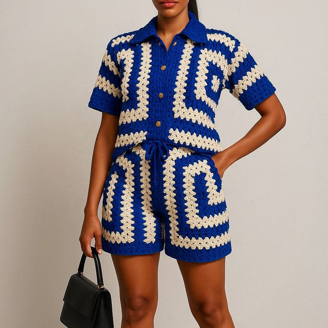Woman wearing a blue and white patterned outfit holding a black handbag against a plain background