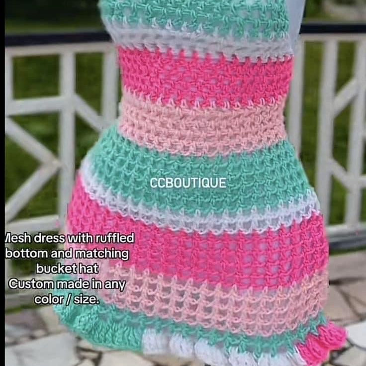 Crocheted dress and matching bucket hat on a mannequin with a blurred outdoor background.