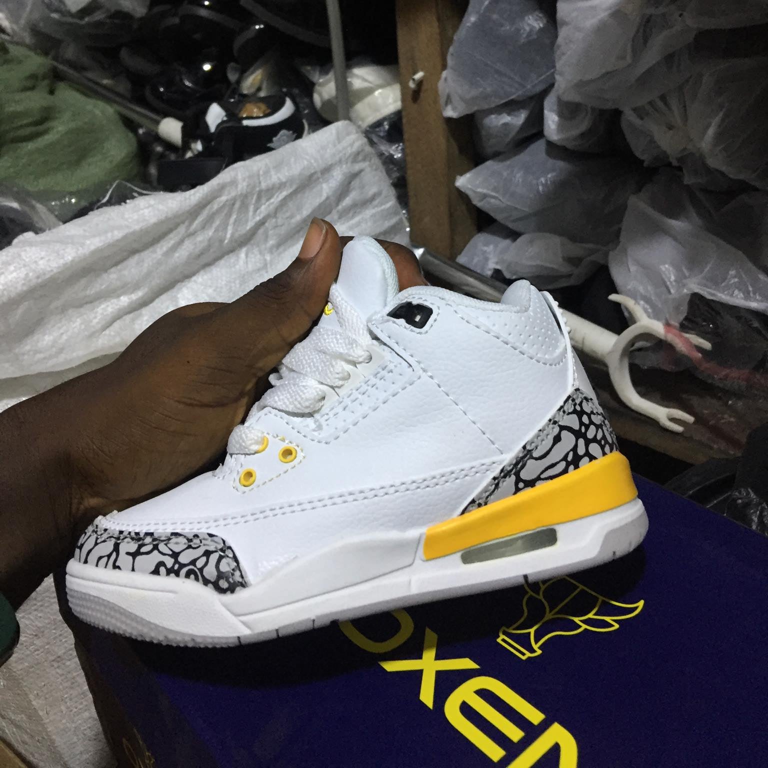 White sneaker with yellow accents held by a hand in a store setting.