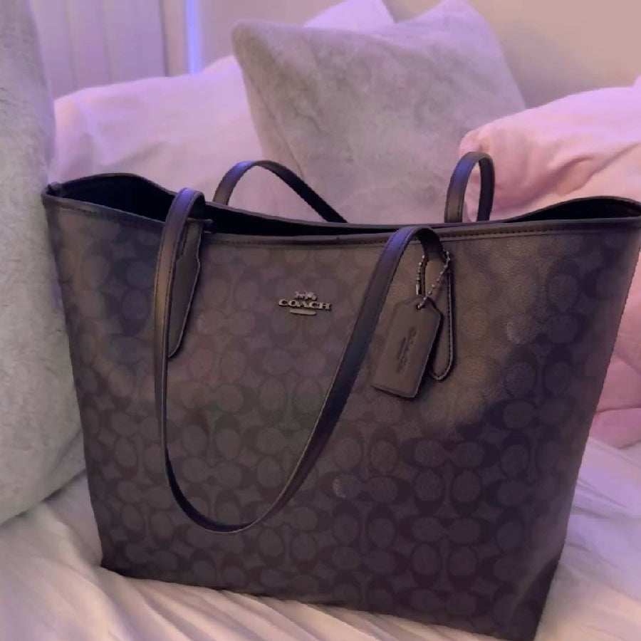 Black patterned handbag on a bed with pillows in the background