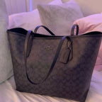 Black patterned handbag on a bed with pillows in the background