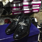 Black shoes with a checkered pattern on a purple surface, with shoe boxes in the background.