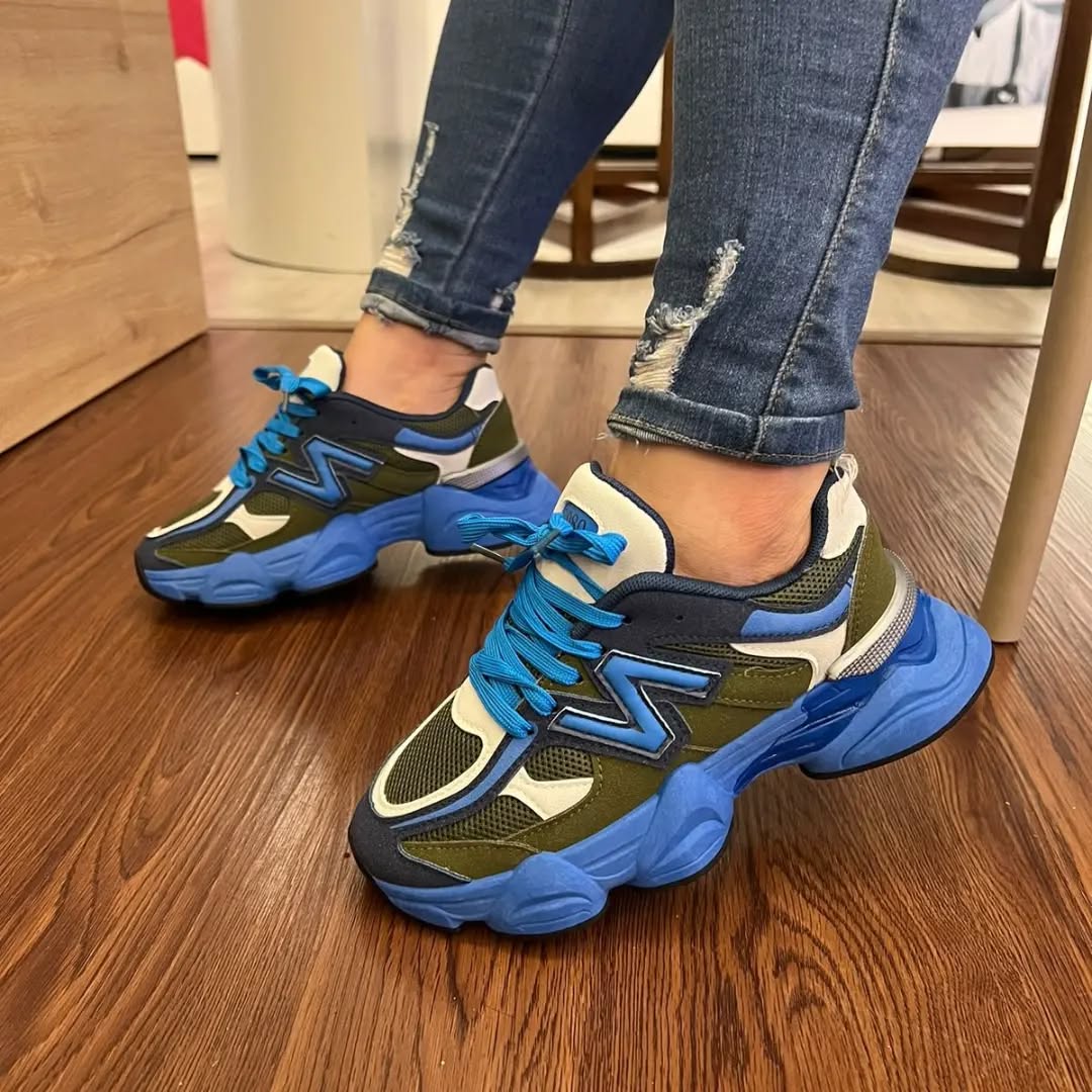 Blue and green sneakers worn with ripped jeans on a wooden floor.