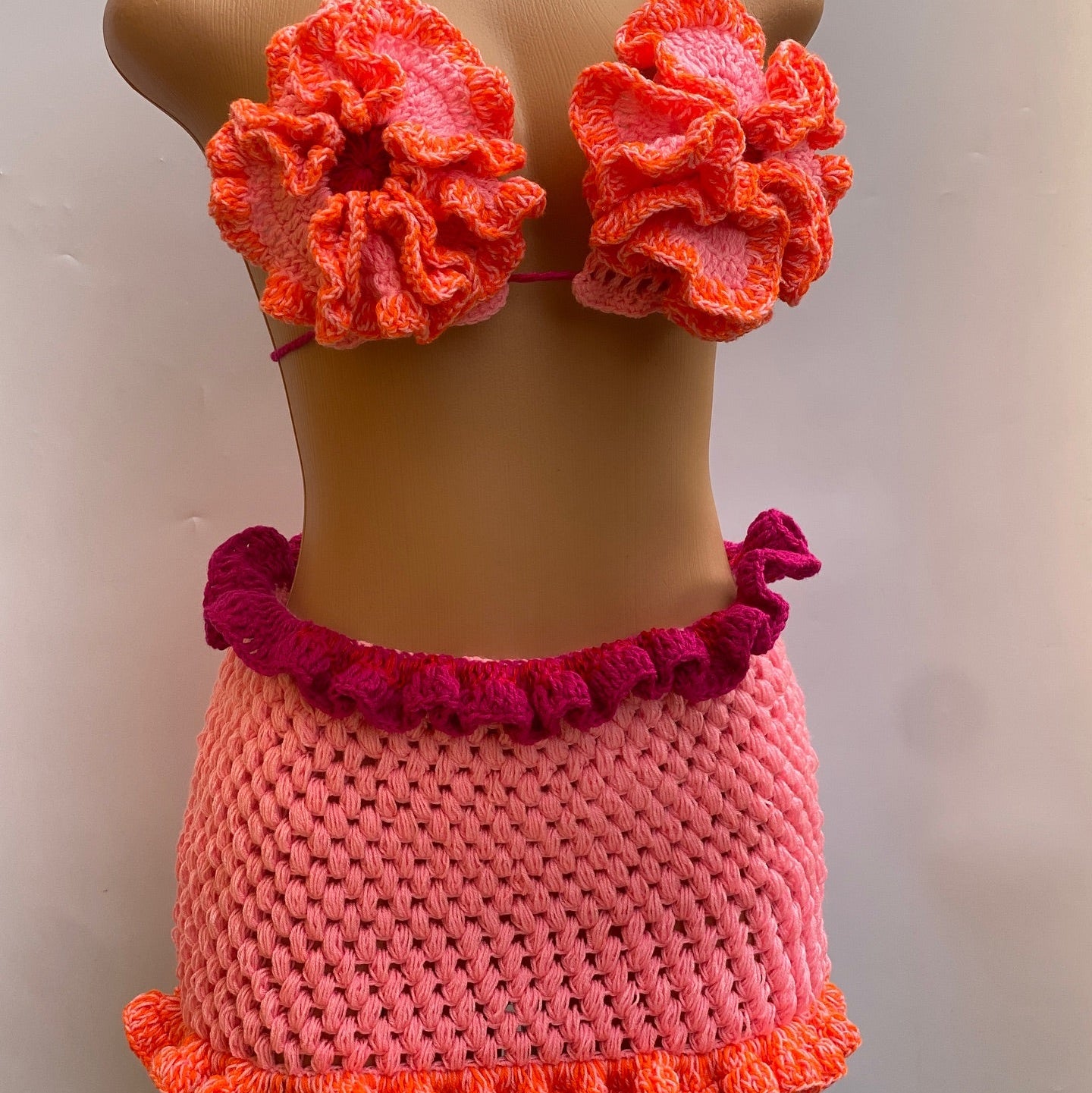 Crocheted bikini set with floral top and ruffled bottom on a mannequin against a plain background