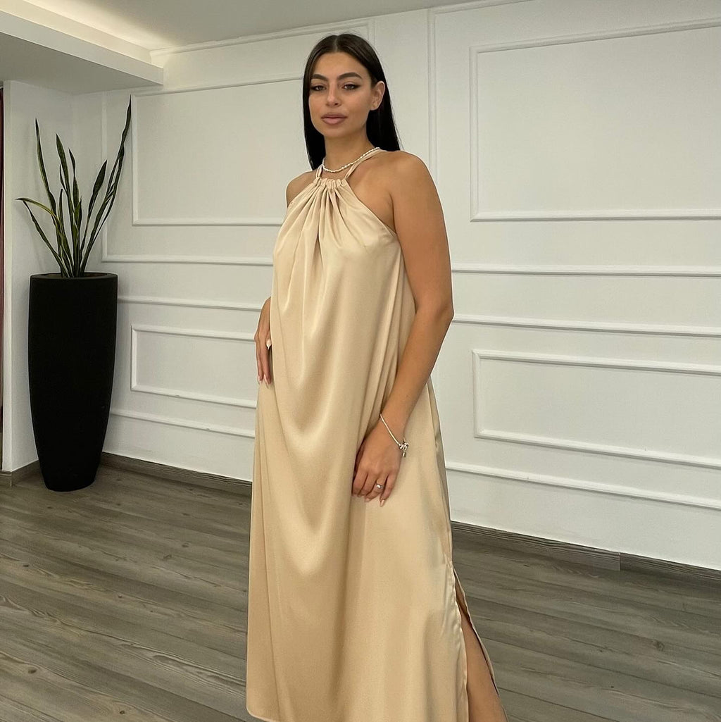 Woman wearing a beige halter neck dress in a room with white paneled walls and a plant.