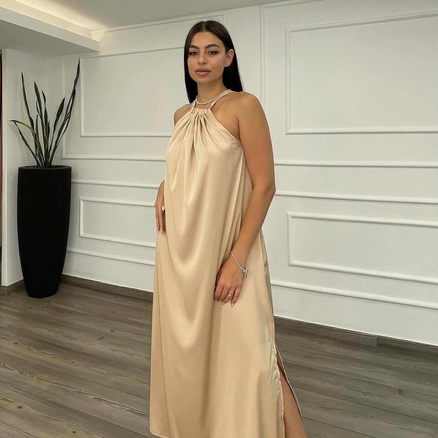 Woman wearing a beige halter neck dress in a room with white paneled walls and a plant.