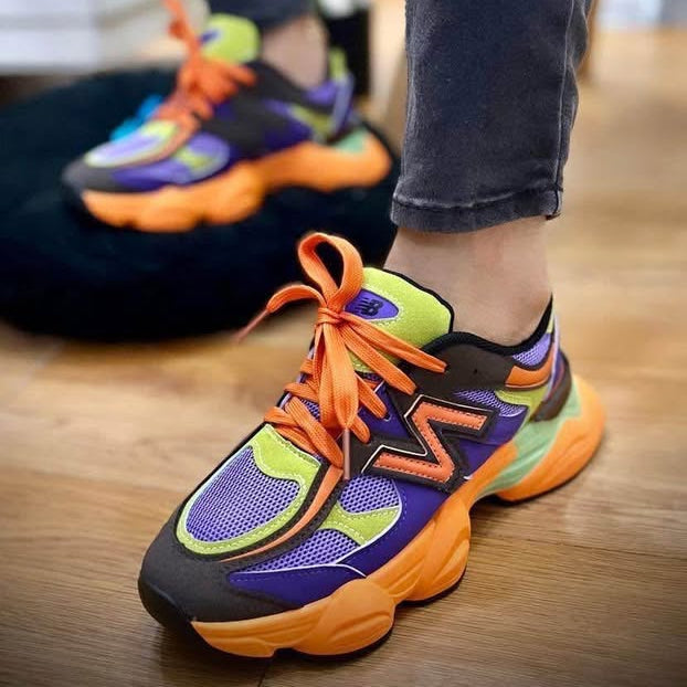 Colorful running shoes with orange laces worn indoors on a wooden floor.