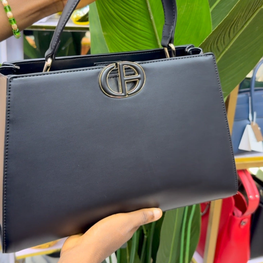 Person holding a dark blue handbag with a brand logo against a green leafy background