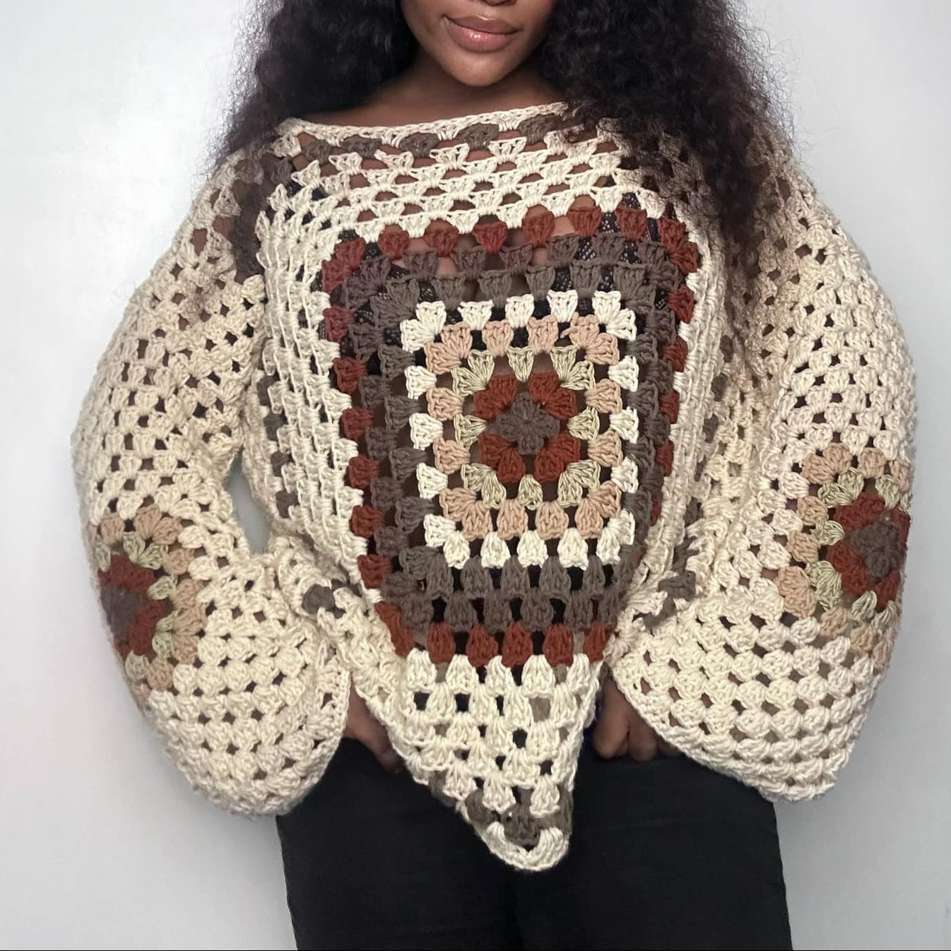 Person wearing a crocheted sweater with a pattern against a plain background