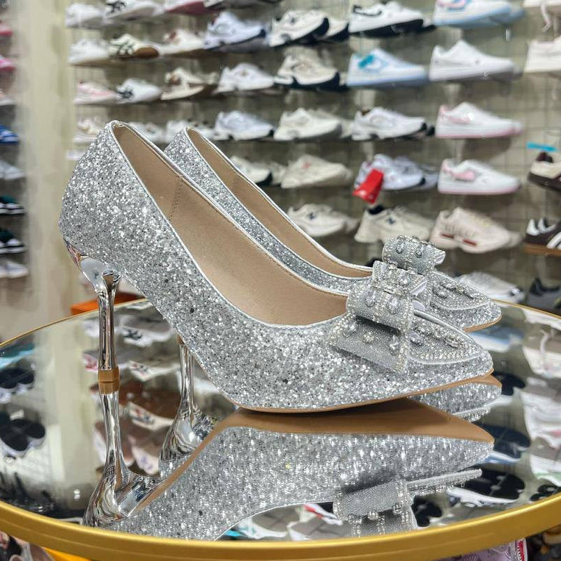 Silver high-heeled shoes with a bow in front of a shoe display wall.