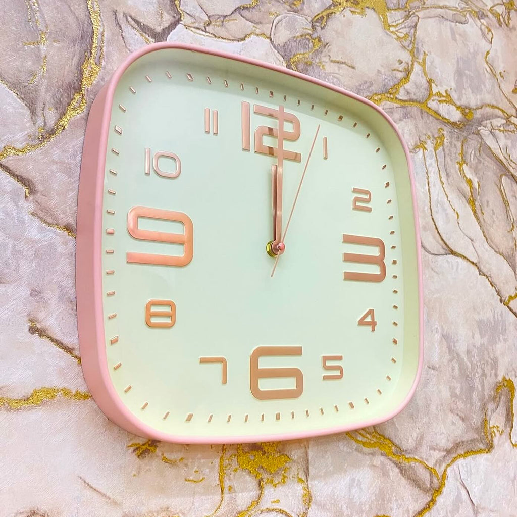 Square wall clock with pink frame and gold numbers on a marble background