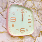 Square wall clock with pink frame and gold numbers on a marble background