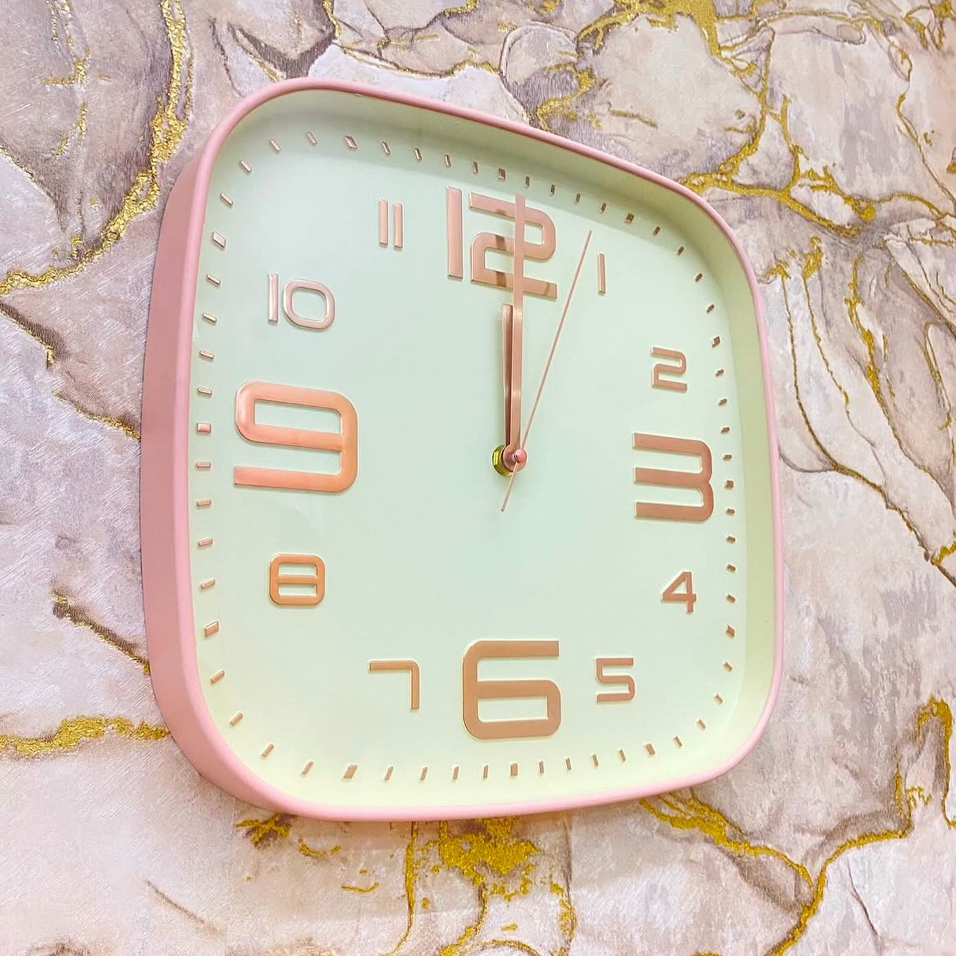 Square wall clock with pink frame and gold numbers on a marble background