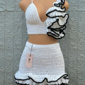 Mannequin wearing a white crochet outfit with black trim against a textured gray wall.