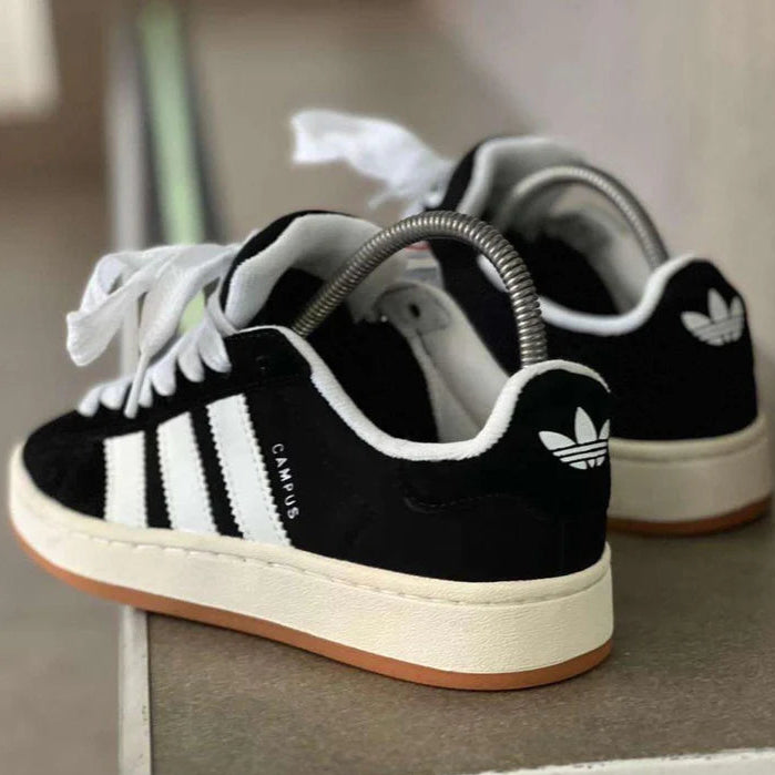 Black Adidas sneakers with white stripes on a neutral background