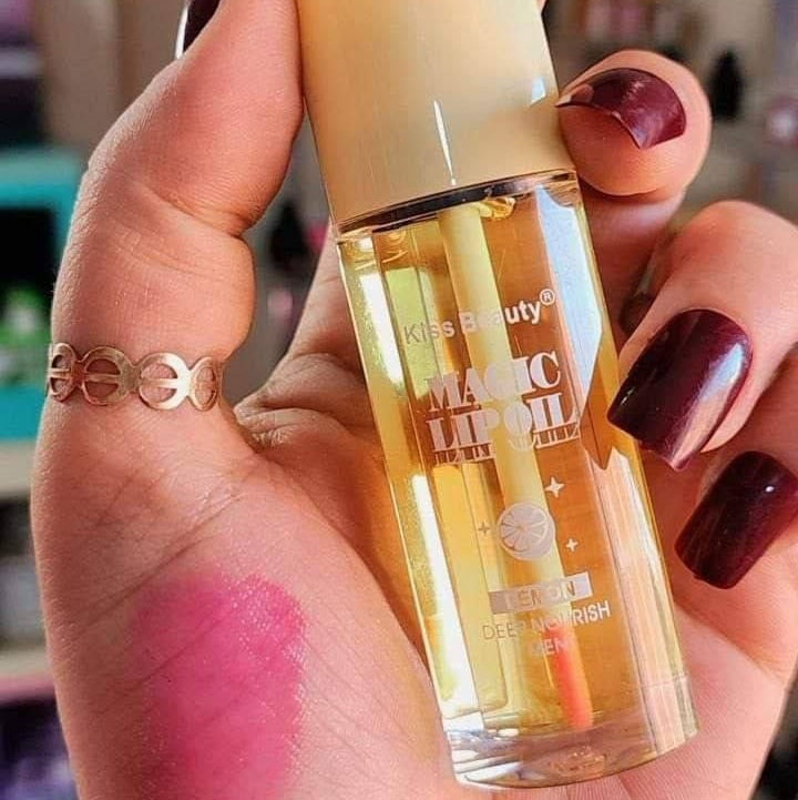 Hand holding a bottle of Kiss Beauty Magic Lip Oil with a blurred background