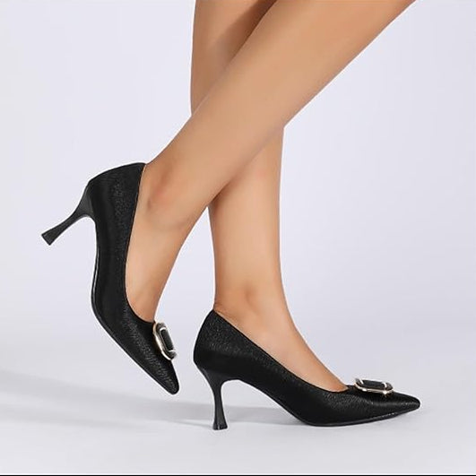 Black high-heeled shoes with a bow detail worn by a person on a light gray background