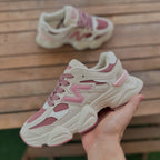 Beige and pink sneakers with a hand holding one shoe on a wooden surface.