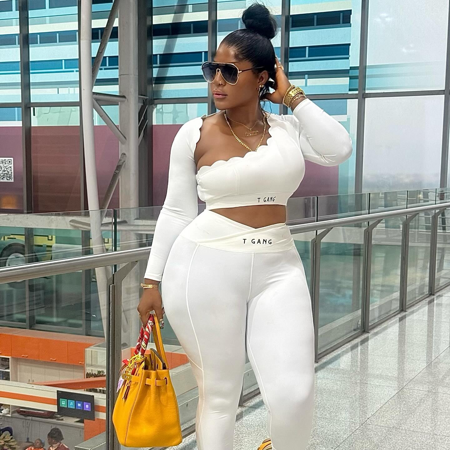 Woman in a white outfit with a yellow handbag walking in an indoor setting.