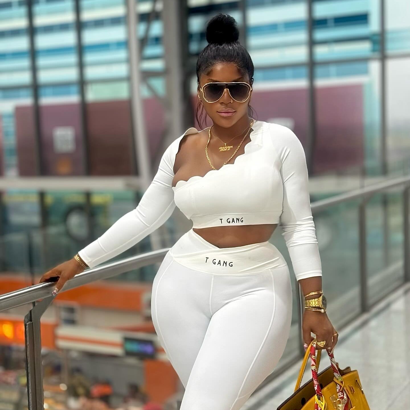 Woman in a white outfit with 'I GAN' text, holding a yellow handbag in an indoor setting.