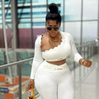 Woman in a white outfit with 'T Gang' branding, holding a yellow bag in an indoor setting.