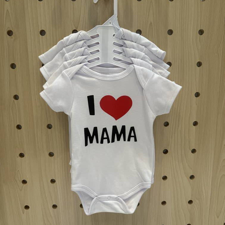 White baby onesie with 'I ❤️ MAMA' text on a wooden pegboard background