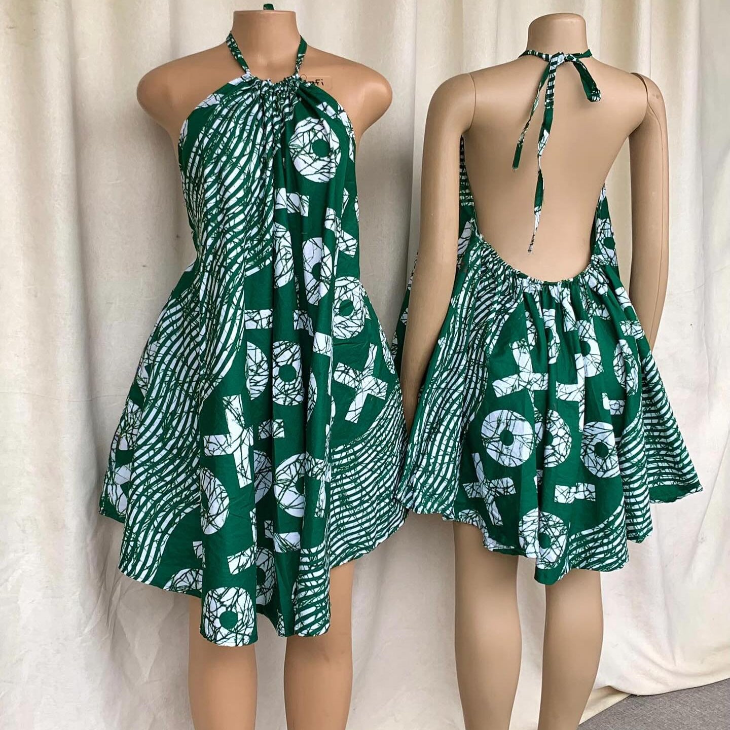 Green and white patterned dress on a mannequin against a white curtain background
