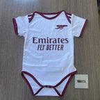 White baby onesie with red accents and 'Emirates Fly Better' text on a wooden surface.