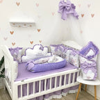 Baby crib with purple and white bedding set in a nursery with heart-patterned wallpaper.