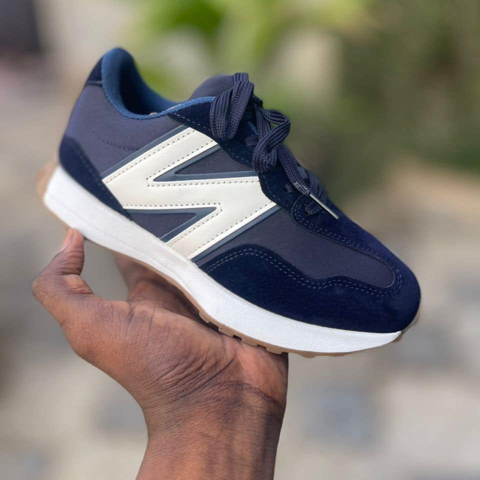 Navy blue sneaker with white accents held in a hand against a blurred natural background
