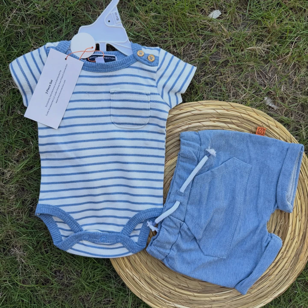 Blue striped baby romper and pants on a hanger with a tag, placed on a woven basket on grass.