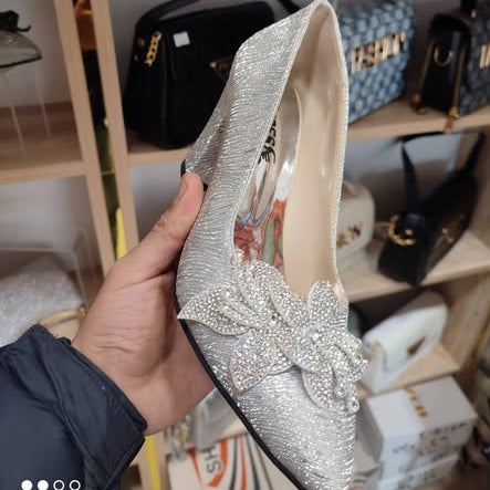 Silver studded shoe held by a hand with a blurred background of bags and boxes.