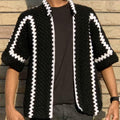 Person wearing a black and white patterned knitted cardigan against a wooden background