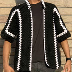 Person wearing a black and white patterned knitted cardigan against a wooden background