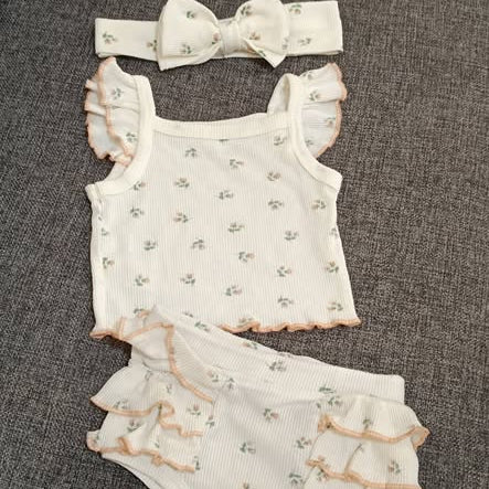 Baby romper set with ruffled details and matching headband on a textured surface
