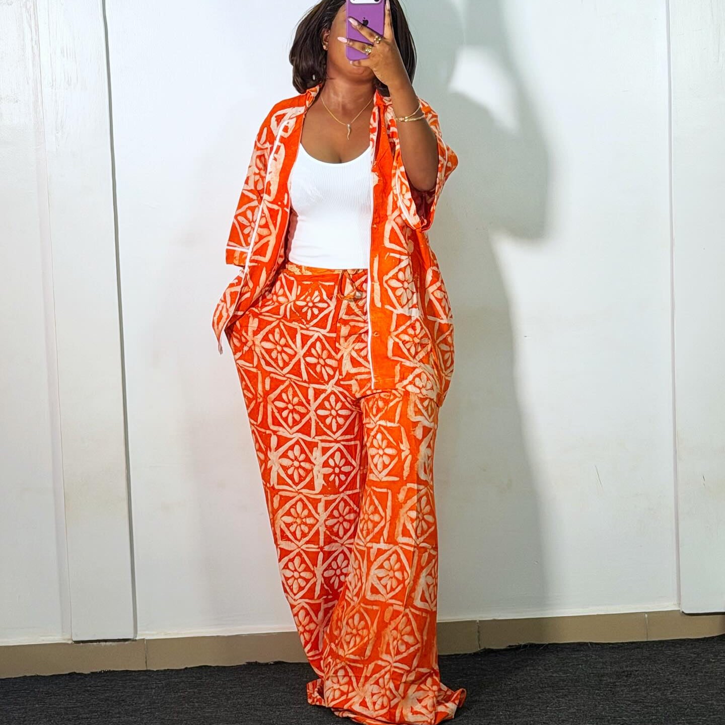 Person wearing an orange and white patterned outfit in front of a white wall with 'Amika' branding.