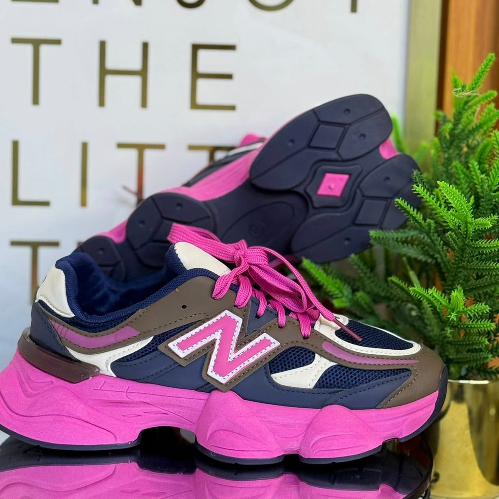 Pink and navy sneakers with a 'New Balance' logo on a reflective surface, with a decorative background.