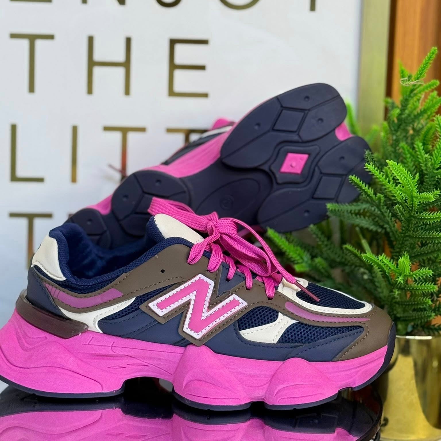 Pink and navy sneakers with a 'New Balance' logo on a reflective surface, with a decorative background.