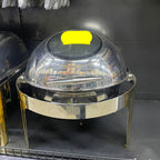 Metallic chafing dish with a clear dome lid on a gray shelf.