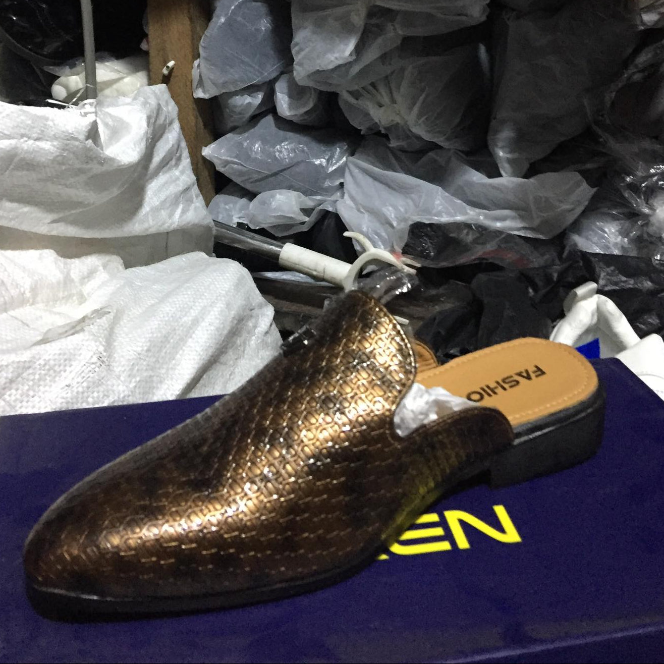 Gold glittery shoe on a blue surface with other shoes in the background.