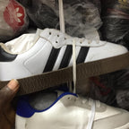 White Adidas sneakers with black stripes held above a pile of shoes in plastic bags.