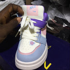 Blue and white sneaker with pink accents held by a hand, brand label visible, with blurred background