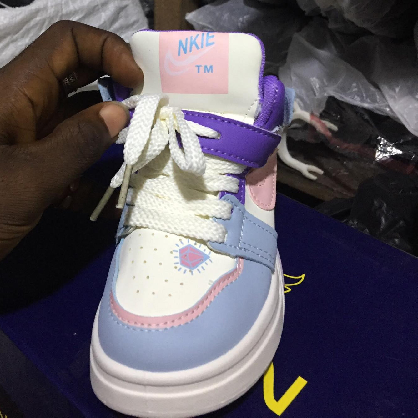 Blue and white sneaker with pink accents held by a hand, brand label visible, with blurred background