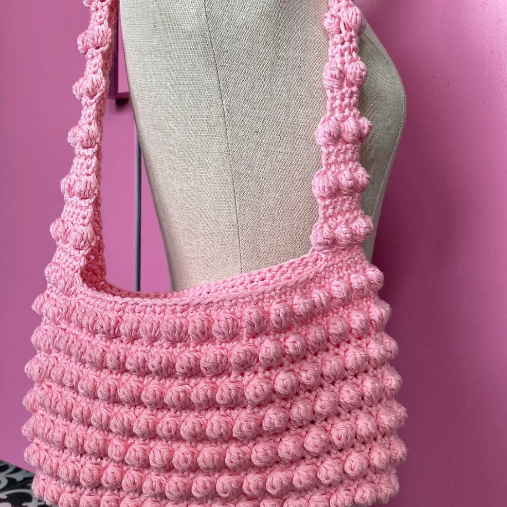 Pink crochet bag on a mannequin against a pink background