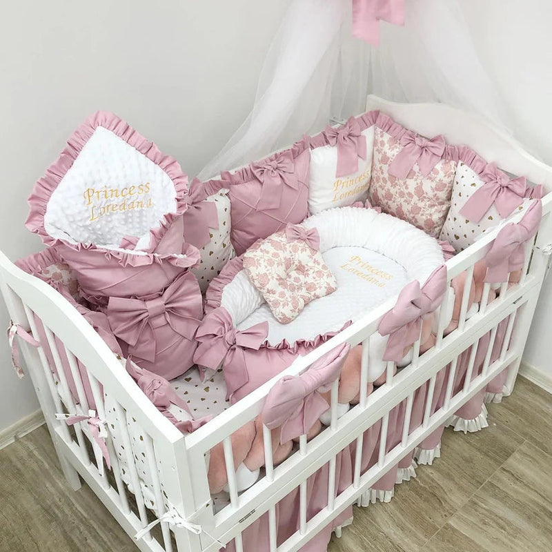 White crib with pink and white baby bedding set, including pillows and a canopy.