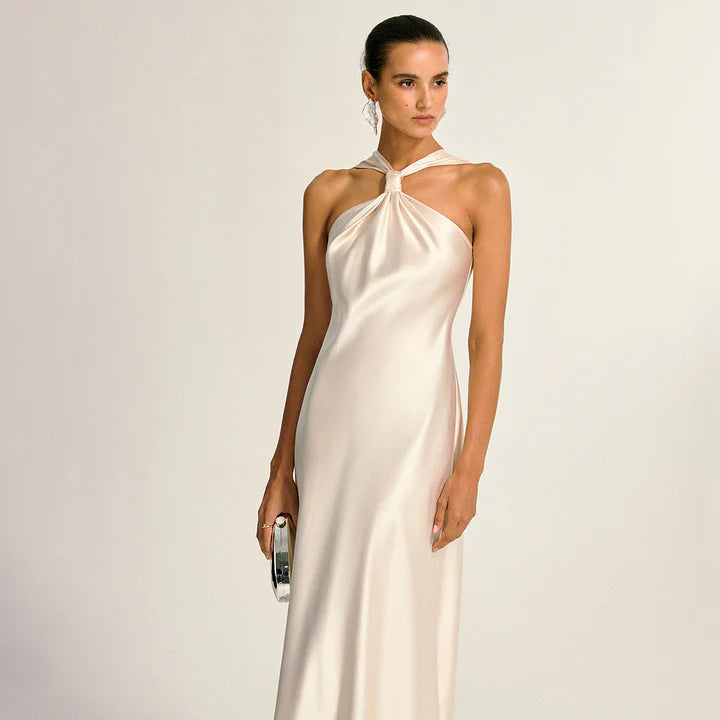 Woman wearing a white halter neck dress against a plain background