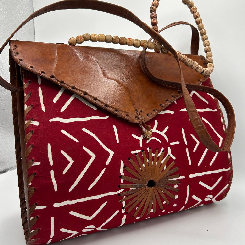 Red patterned handbag with brown leather accents on a white background