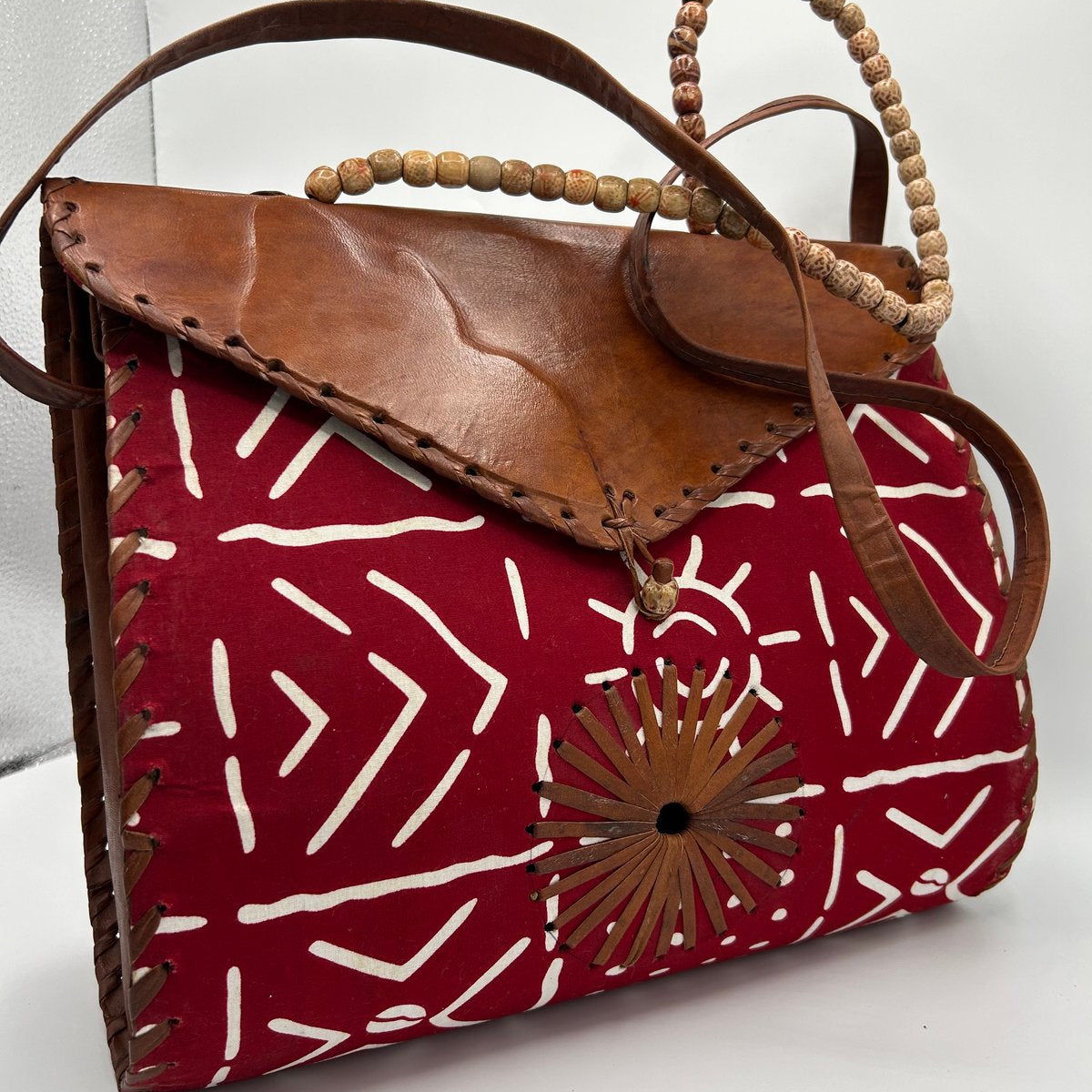 Red patterned handbag with brown leather accents on a white background