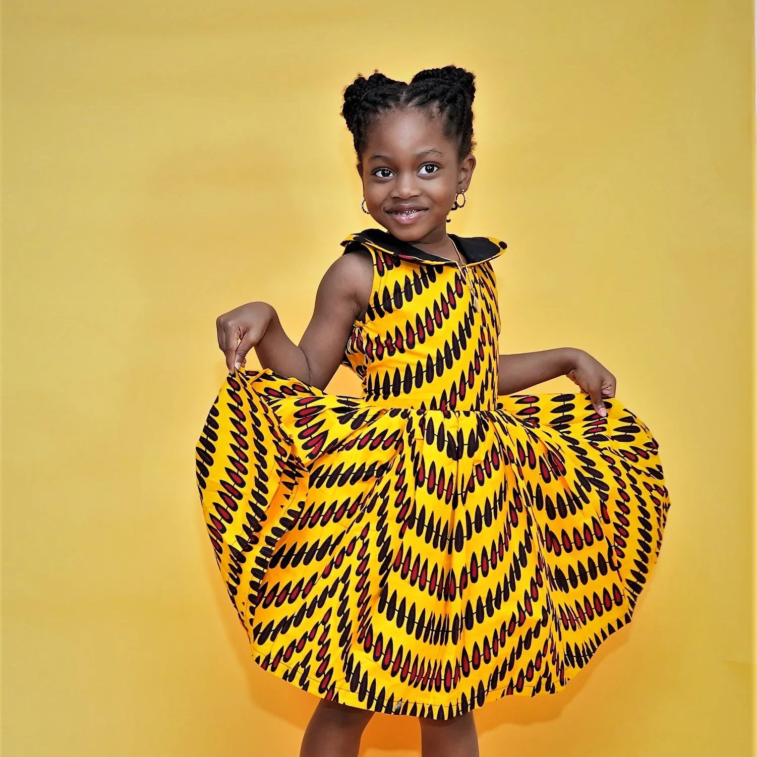 Young girl wearing a yellow and black patterned dress on a yellow background