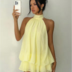 Woman wearing a light yellow halter neck dress against a plain background